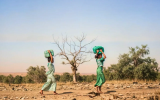 Two women carrying water through a barren land